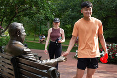 Student shaking hand of Herman B Wells statue on the IU Bloomington campus with another student waiting